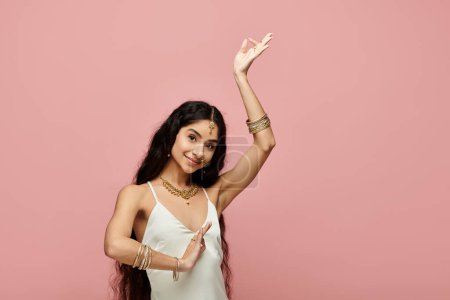 Graceful indian woman in white dress dancing on vibrant pink backdrop.