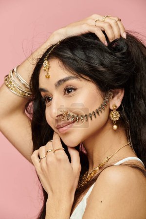 indian woman with gold jewelry strikes a pose on pink background.