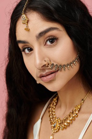 A young indian woman showcases her beauty with gold jewelry and a nose ring.