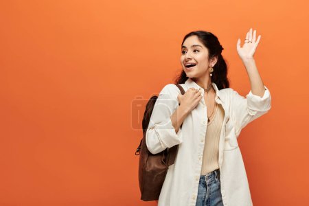 A young indian woman energetically waves hand against orange background.