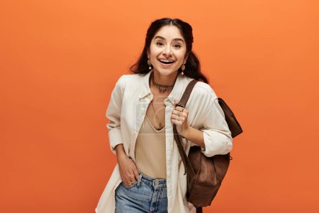 Photo for Smiling indian woman with backpack against vibrant orange backdrop. - Royalty Free Image