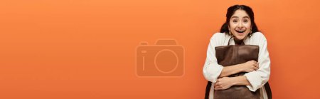 Foto de Joven mujer india sosteniendo bolsa marrón en frente de fondo naranja negrita. - Imagen libre de derechos