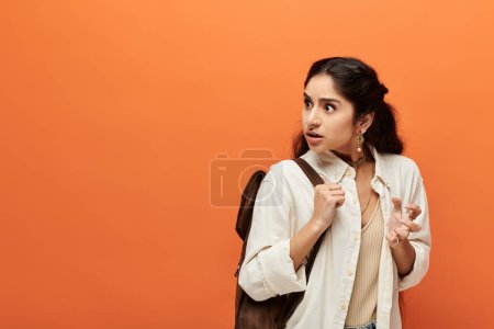 Young indian woman with backpack against orange wall