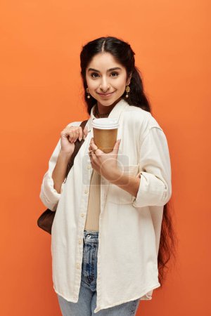 Junge indische Frau genießt Kaffee vor orangefarbener Kulisse.