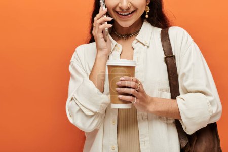 Téléchargez les photos : Une jeune femme indienne bavarde au téléphone tout en dégustant une tasse de café. - en image libre de droit