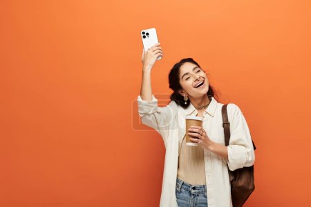 femme indienne capture moment avec téléphone sur fond orange vibrant.