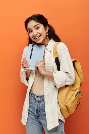 Junge indische Frau hält Notizbuch auf orangefarbenem Hintergrund.