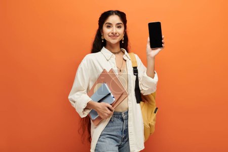 Young indian woman holding phone and backpack in urban setting.