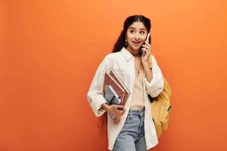 Téléchargez les photos : Jeune femme indienne conversant énergiquement sur téléphone portable sur fond orange gras. - en image libre de droit