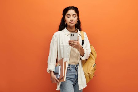 Photo for Young indian woman holding a backpack, looking at her phone. - Royalty Free Image