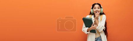Téléchargez les photos : Une femme indienne tient un livre sur un fond orange. - en image libre de droit