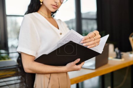 Jeune femme indienne attrayante pose énergiquement tout en tenant un dossier dans un cadre de bureau.