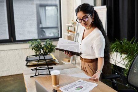 Photo for Young indian woman with glasses working at desk with papers. - Royalty Free Image