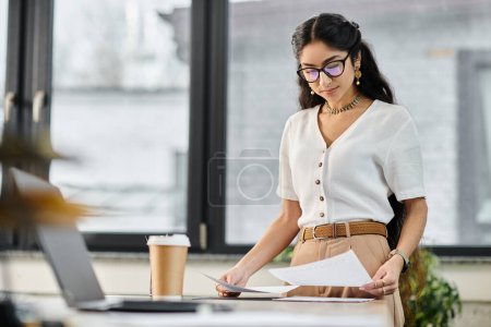 Téléchargez les photos : Une femme indienne dans des lunettes se tient à un bureau avec des papiers. - en image libre de droit