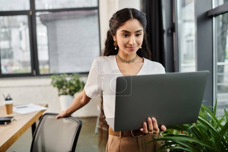 Photo for A focused young indian woman working meticulously on her laptop in a modern office. - Royalty Free Image