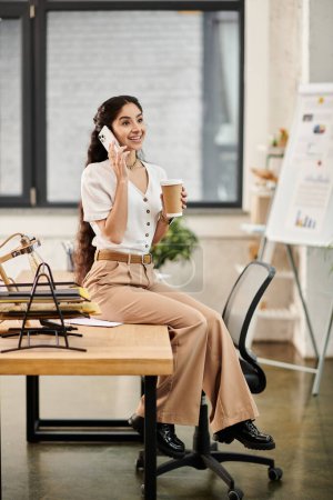 Jeune femme indienne au bureau, parlant animément au téléphone.