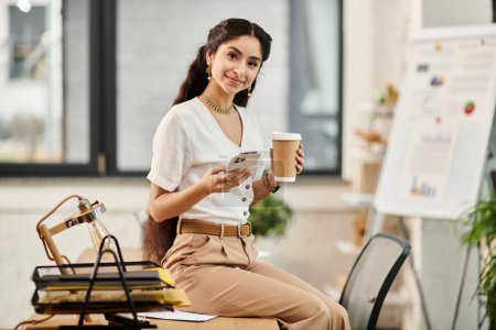 Eine junge Indianerin sitzt an einem Schreibtisch und hält elegant eine Tasse Kaffee.