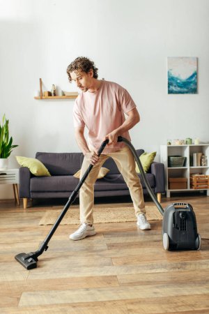 Hombre en ropa de casa acogedora utiliza el vacío para limpiar el suelo.
