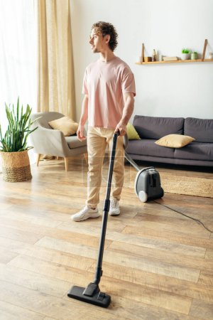 Handsome man in cozy homewear vacuuming on hardwood floor.
