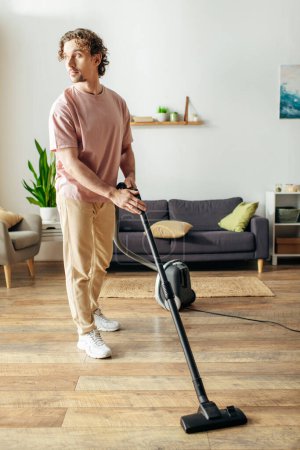Ein gutaussehender Mann in gemütlicher Hauskleidung saugt seinen Wohnzimmerboden.
