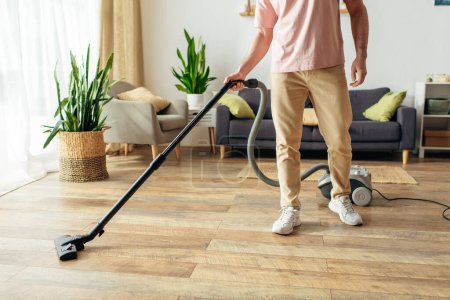 Foto de Un hombre guapo en ropa de casa acogedora usando un vacío para limpiar el piso. - Imagen libre de derechos