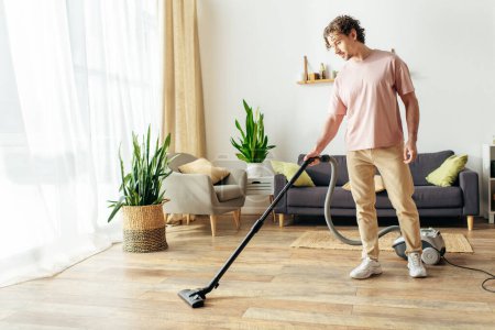 Ein gutaussehender Mann in gemütlicher Hauskleidung benutzt einen Staubsauger, um ein Wohnzimmer zu säubern.
