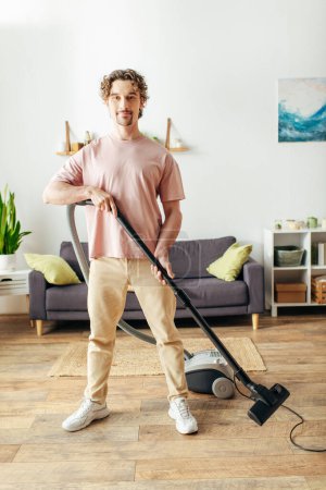A man in cozy homewear stands in a living room, confidently holding a vacuum.