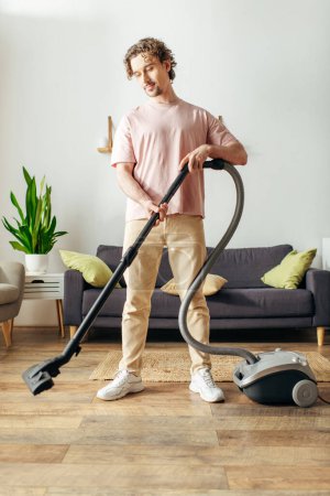 Téléchargez les photos : Un bel homme en tenue confortable à l'aide d'un aspirateur pour nettoyer le sol. - en image libre de droit