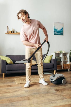 Photo for A handsome man in cozy homewear diligently vacuums his living room. - Royalty Free Image