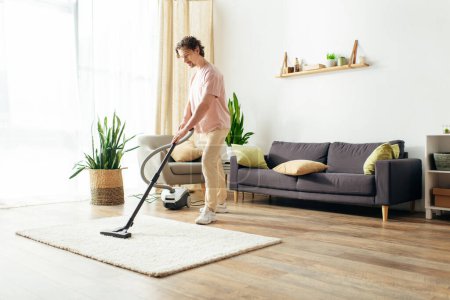 Photo for A handsome man in cozy homewear cleans his house using a vacuum cleaner. - Royalty Free Image