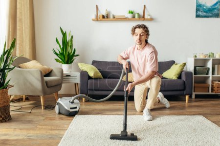 Foto de A handsome man in cozy homewear diligently vacuuming a living room. - Imagen libre de derechos