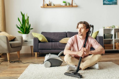 A handsome man in cozy homewear sitting on the floor while vacuuming.