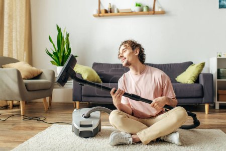 Téléchargez les photos : A handsome man in cozy attire sits on the floor next to a vacuum cleaner. - en image libre de droit
