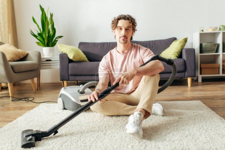 Photo for A handsome man in cozy homewear sits on the floor with a vacuum. - Royalty Free Image