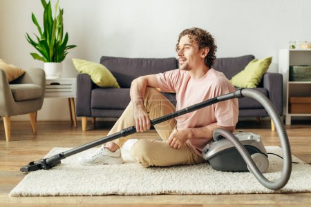 A handsome man sitting on the floor serenely while using a vacuum cleaner in cozy homewear.