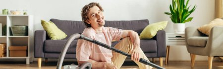 A man in cozy homewear sits on the floor with a vacuum.