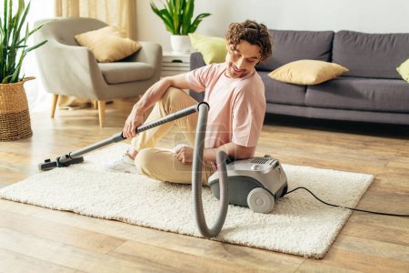 Handsome man in cozy homewear using a vacuum to clean a living room.