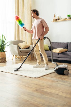 A handsome man in cozy homewear diligently vacuums the living room.