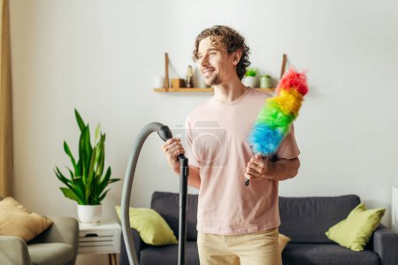 A stylish man holding a colorful toy next to a vacuum cleaner in a cozy home.