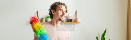 Photo for A handsome man in cozy homewear holds a multicolored duster. - Royalty Free Image