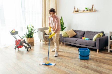 Photo for Handsome man in cozy homewear cleaning his living room with a mop. - Royalty Free Image