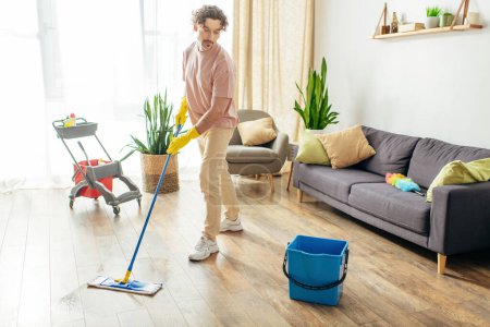 Téléchargez les photos : Beau homme dans des vêtements confortables à la maison en nettoyant gracieusement le sol. - en image libre de droit