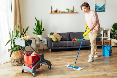 Un hombre con estilo en acogedora ropa de casa meticulosamente limpia el suelo.