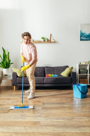 Handsome man in cozy homewear cleaning floor with mop.
