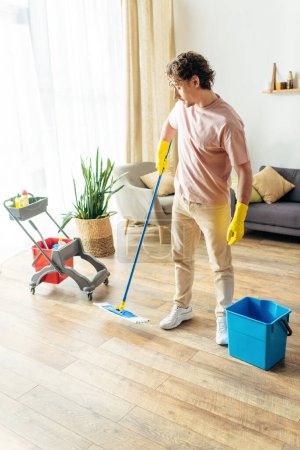 Hombre guapo en ropa de casa acogedora fregar y limpiar una sala de estar.