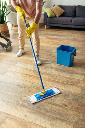 Photo for A handsome man in cozy homewear diligently mopping the floor. - Royalty Free Image