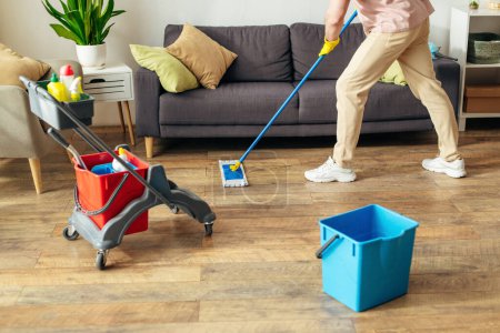 Téléchargez les photos : Un homme en action, nettoyer le sol avec une serpillière dans un cadre confortable à la maison. - en image libre de droit