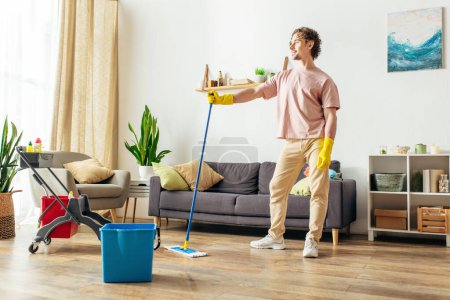 Ein gutaussehender Mann in kuscheliger Hauskleidung putzt das Wohnzimmer mit Wischmopp und Eimer.
