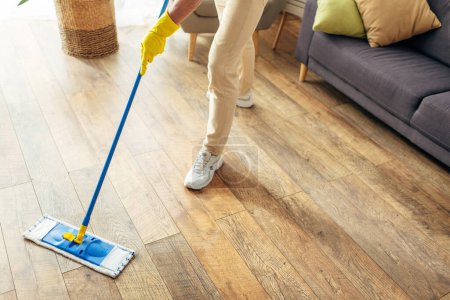 Photo for A handsome man in cozy homewear cleans a wooden floor with a mop. - Royalty Free Image