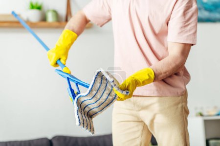 A man in cozy homewear meticulously mops the living room floor.